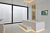 Designer bathtub with step and indirect lighting in minimalist, white, designer bathroom