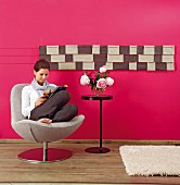 DIY wall hanging made from leather remnants on hot pink wall; woman sitting on chair reading