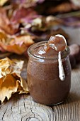 Chestnut cream in a jar on a wooden surface with autumnal leaves