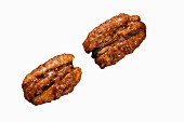 Two roasted pecan nuts on a white surface