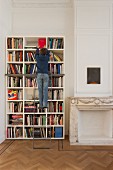 Junge auf Bibliotheksleiter vor Bücherregal neben Kamin mit Marmorverkleidung