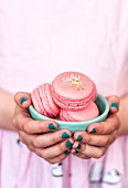 A little girl holding a bowl of raspberry macaroons with sprinkles