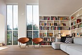 Retro leather shell chairs in front of tall windows, bookcases and grey sofa in living room