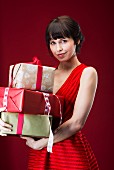 Dark-haired woman wearing red sleeveless dress holding wrapped gifts