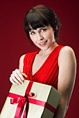 Dunkelhaarige Frau in rotem, ärmellosem Kleid mit Geschenkpaket in der Hand