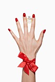 Frauenhände mit rot lackierten Fingernägeln halten Parfümfläschchen