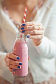 A woman holding a glass bottle of vegan raspberry milk shake
