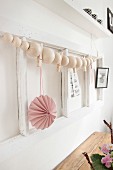 String of wooden beads and pink paper pendant on white wooden frame