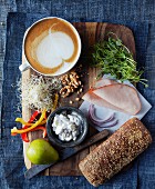 Ingredients for a turkey sandwich (turkey ham, pears, cottage cheese, pepper, walnuts, alfalfa sprouts and red onions) with a cafe latte