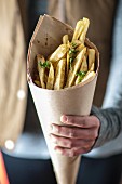 Person hält Spitztüte aus Papier mit Kräuter-Pommes