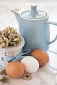 Hen's eggs with a ribbon, a hydrangea and a blue coffee pot on a marble surface
