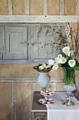Weisser Tulpenstrauss und Etagere mit Gebäck auf Wandtisch, vor rustikaler Wand