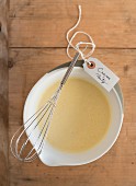 Crêpe batter in a bowl with a whisk and a label for a party