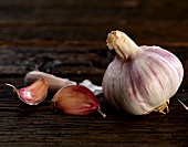 A bulb of garlic and some garlic cloves on a wooden surface