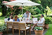 Gartenfeier mit Gästen an gedecktem Tisch mit integriertem Sonnenschirm