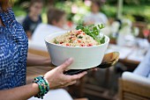 Woman holding white bowl of couscous salad