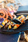 Skewers on a barbecue being turned with a pair of tongs