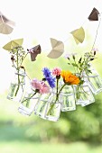 Paper garland and garland of small glass bottles holding summer flowers