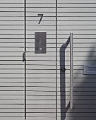 Modern front door made from grey wooden panels with metal bar handle (detail)