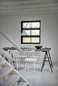 Simple dining area with white-painted chairs around wooden table on metal trestles