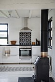 Cast iron log burner in simple kitchen with vintage tiled splashback above cooker integrated in kitchen counter
