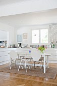 Various white chairs around dining table in open-plan modern fitted kitchen