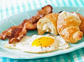 A fried egg with bacon and a croissant