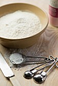 A bowl of flour with measuring spoons next to it