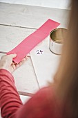 Tin can, sticker and pink paper in girl's hand for making DIY Advent calendar