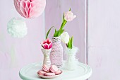 Tulips in vases wrapped in cord next to plate of pink macarons