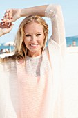 A blonde woman on the beach wearing a see-through woollen jumper