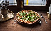 Pizza with avocado and rocket on a wooden table in front of a window in a restaurant