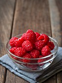 Fresh raspberries in a glass bowl on a wooden surface