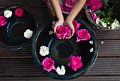 Schwimmende Rosenblüten in Keramikschale, Mädchenhände halten pinkfarbene Blüte