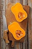 A halved butternut squash on a chopping board with a knife