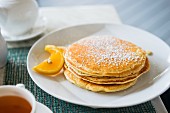 A stack of pancakes dusted with icing sugar and serve with orange slices