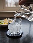 Person giesst Sodawasser in Cocktailglas mit Wodka und Eiswürfeln