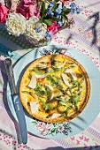 Quiche with green asparagus, ham and rocket on a table outside