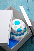 A spotted, two-tier cake in a transportation box