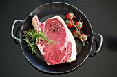 Cote de boeuf in a cast iron pan with tomatoes, rosemary and peppercorns