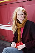 A blond woman wearing a pink blouse and a woollen jacket with a scarf