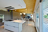 View from kitchen through glass partition wall into open-plan living area with wooden ceiling