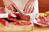 A man slicing a rectangular salami for a cold cuts platter