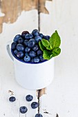 Blueberries and peppermint leaves in a white enamel cup