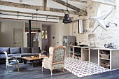 Offener Wohnraum mit antikem Sessel und Stuhl um Couchtisch, dunkelgrauem Sofa und Küchenzeile