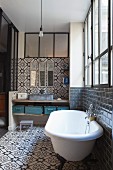 Ornate tiles, free-standing bathtub, industrial window and rustic washstand with metal containers on shelf in bathroom