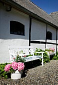 Weiß lackierte Sitzbank mit blühenden Hortensien vor traditionellem Landhaus mit sichtbarem Fachwerk