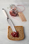 A slice of rye bread with a knife and strawberry jam