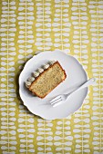 A slice of lemon and poppyseed cake with cream cheese frosting on white plate with a fork