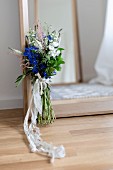 Bunch of wild flowers with lace ribbon leaning against mirror on floor